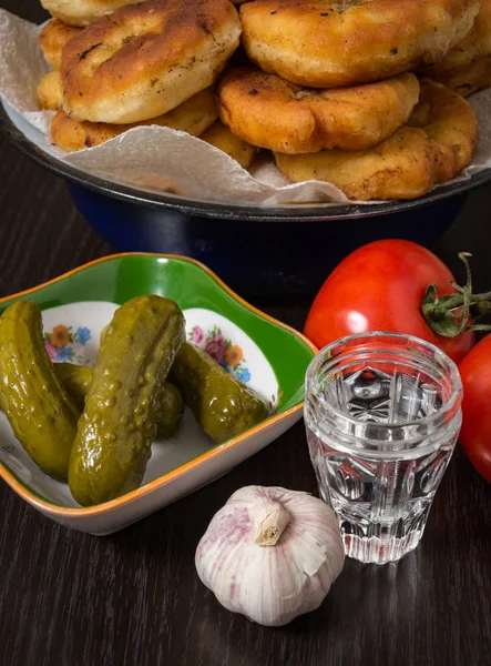 Belyashi, rajčata, nakládané okurky, česnek, sklenice s vodkou — Stock fotografie