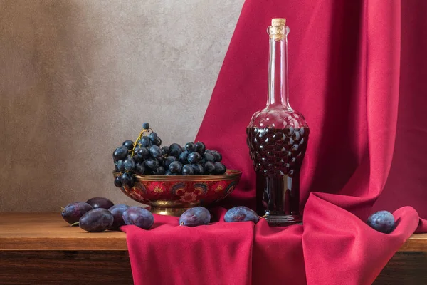 Натюрморт с виноградом и сливами на фоне темно-красной драпировки — стоковое фото