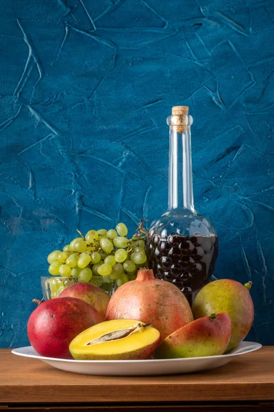 Манго, гранат, виноград і пляшка вина. Натюрморт на синьому фоні — стокове фото