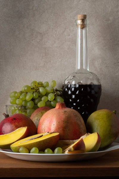 Mango, Granatapfel, Trauben und eine Flasche Wein. Stillleben auf grauem Hintergrund — Stockfoto