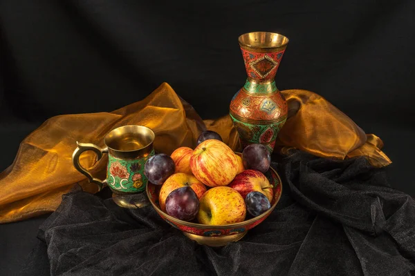 Still life with plums and apples on a dark background.