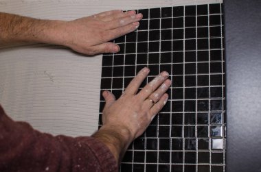 Ev onarım: duvara mozaik çini yükleme. Bir işçi duvar çentikli bir mala kullanarak yapıştırıcı ile kapsar..