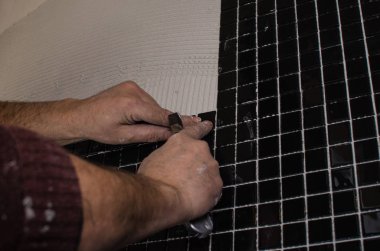 Ev onarım: duvara mozaik çini yükleme. Bir işçi duvar çentikli bir mala kullanarak yapıştırıcı ile kapsar..