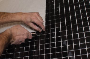 Ev onarım: duvara mozaik çini yükleme. Bir işçi duvar çentikli bir mala kullanarak yapıştırıcı ile kapsar..