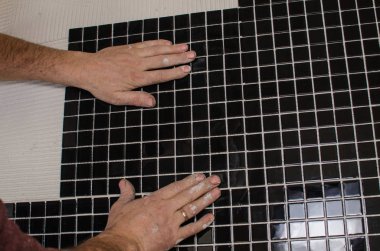 Ev onarım: duvara mozaik çini yükleme. Bir işçi duvar çentikli bir mala kullanarak yapıştırıcı ile kapsar..