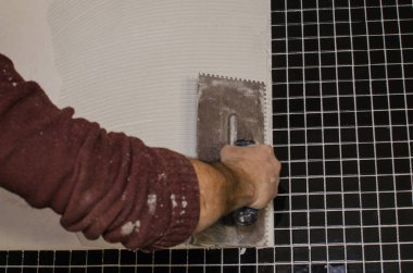 Ev onarım: duvara mozaik çini yükleme. Bir işçi duvar çentikli bir mala kullanarak yapıştırıcı ile kapsar..