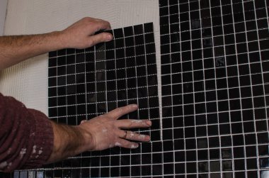 Ev onarım: duvara mozaik çini yükleme. Bir işçi duvar çentikli bir mala kullanarak yapıştırıcı ile kapsar..