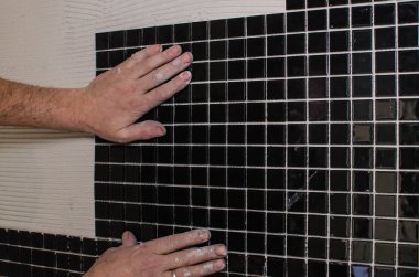 Ev onarım: duvara mozaik çini yükleme. Bir işçi duvar çentikli bir mala kullanarak yapıştırıcı ile kapsar..