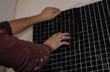 Ev onarım: duvara mozaik çini yükleme. Bir işçi duvar çentikli bir mala kullanarak yapıştırıcı ile kapsar..