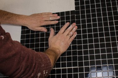 Ev onarım: duvara mozaik çini yükleme. Bir işçi duvar çentikli bir mala kullanarak yapıştırıcı ile kapsar..