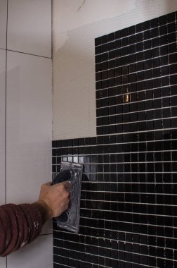 Ev onarım: duvara mozaik çini yükleme. Bir işçi duvar çentikli bir mala kullanarak yapıştırıcı ile kapsar..