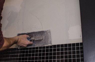 Ev onarım: duvara mozaik çini yükleme. Bir işçi duvar çentikli bir mala kullanarak yapıştırıcı ile kapsar..