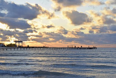 Ufukta insanların olduğu çok renkli bulutlar, deniz ve iskele boyunca güzel bir gün batımı.. 
