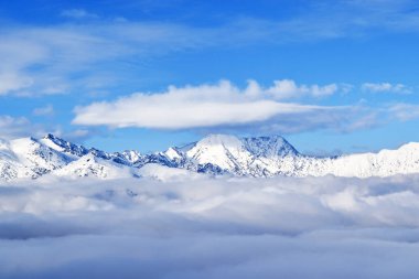 Karlı dağların ve aşağıdaki kabarık bulutların üzerinde mavi bir gökyüzüne doğru uçan beyaz bir bulutun görüntüsü