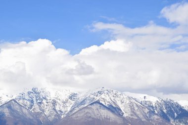 Güzel kümülüs manzarası, beyaz, büyük bulutlar dağların karlı zirvesinde mavi gökyüzüne karşı.