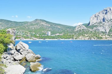  Mavi denizin güzel manzarası, yüksek yeşil dağlar ve büyük taşlar.