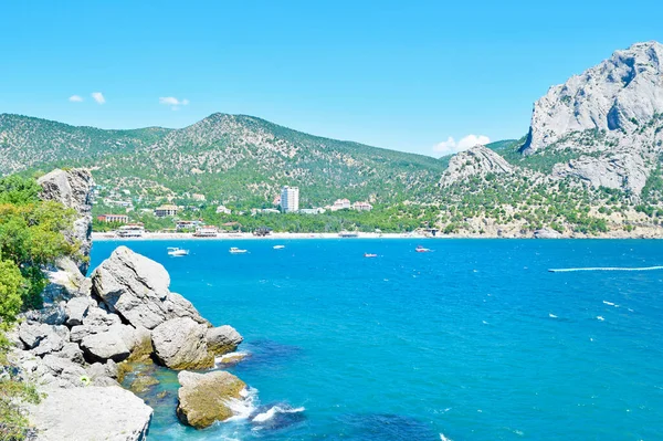 Mavi denizin güzel manzarası, yüksek yeşil dağlar ve büyük taşlar.