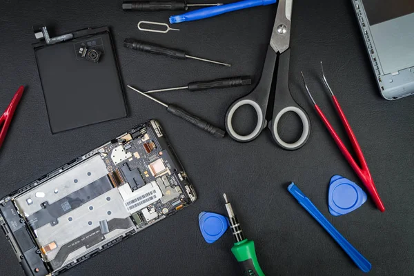 Bozukluğu tamirci detayları smartphone ve özel araçları ile siyah bir tablo üzerinde. Flatlay tarzı sökülüp telefon.