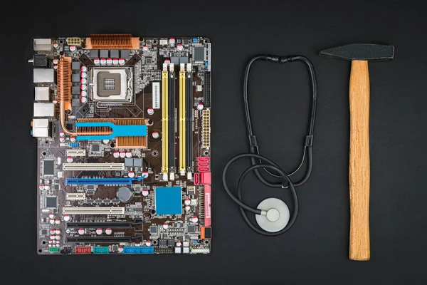 Repair or crash the computer. Broken motherboard, hammer and stethoscope on a black table. Flat lay