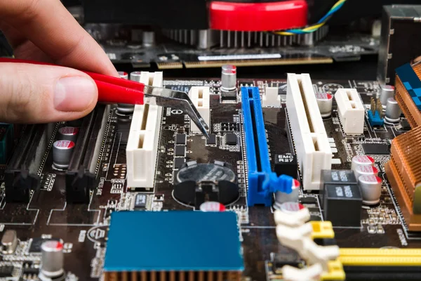 Fix and restore the old game motherboard with tweezers on a black table. Workplace repairman computers.