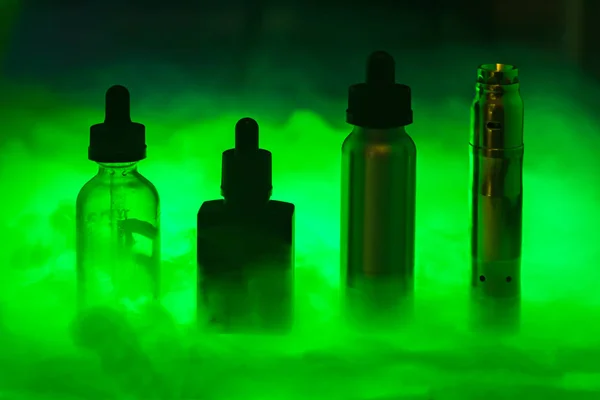 E sigara duman koyu yeşil arka plan üzerinde üç e-sıvı ile. E-suyu vape rengi. Alternatif sigara