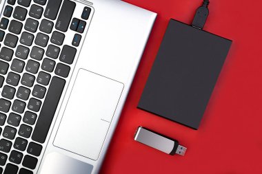 Laptop ile harici sabit disk ve flash sürücüde kırmızı bir arka plan, üstten görünüm parçası. Mobil veri depolama kavramı