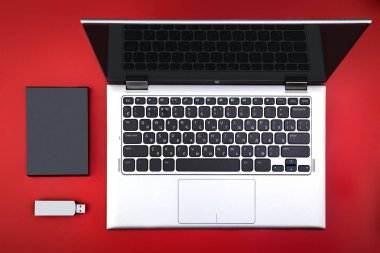Bir flash sürücü, harici sabit disk ve kırmızı masa üstünde açık bir laptop. Mobil veri depolama kavramı. Düz yatıyordu