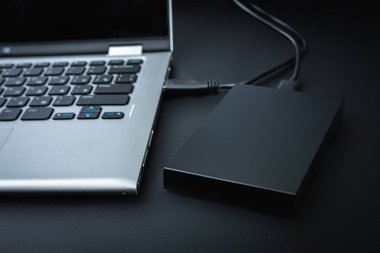 Harici sabit disk siyah bir tablo üzerinde bir usb kablosu ile dizüstü bilgisayara bağlı. Taşınabilir depolama teknolojileri