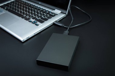 Harici sabit disk siyah bir arka plan üzerinde bir usb kablosu ile dizüstü bilgisayara bağlı. Taşınabilir depolama teknolojileri
