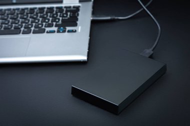 Bir harici hdd siyah bir tablo üzerinde bir usb kablosu ile dizüstü bilgisayara bağlı. Taşınabilir depolama teknolojileri