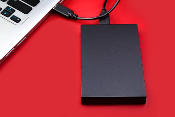 An external hdd connected to the laptop with a usb cable on a red table. Portable storage technologies