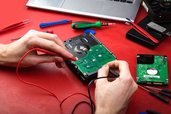 The process of repairing a hard drive with parts, a laptop and special tools on a red table. Work of the repairman