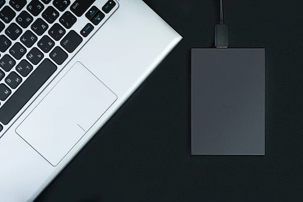 The concept of data storage. A portable hdd connected to a laptop with usb flash drive on a black table, flat lay.