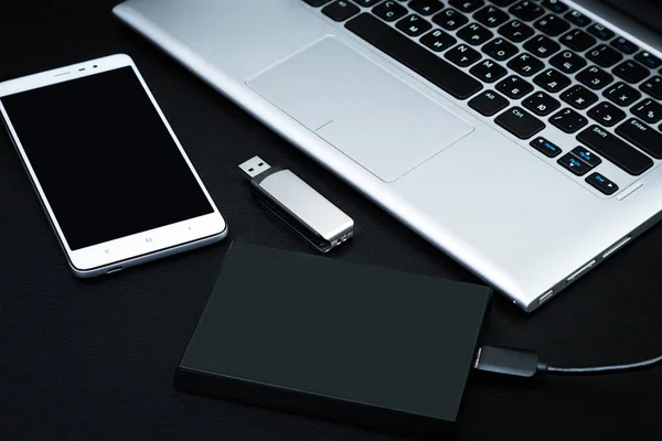 External hard drive connected to the laptop, USB flash drive and smartphone on a black background. The concept of mobile technology