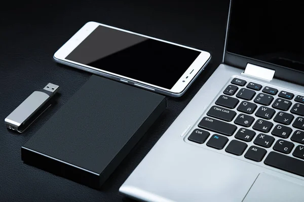 External hdd with the laptop, USB flash drive and smartphone on a black background. The concept of portable data storage