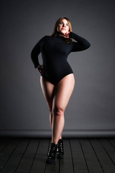 Plus size sexy model in black bodysuit, fat woman on gray studio background, overweight female body, full length portrait