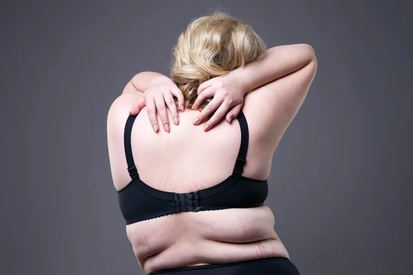 Back and neck pain, fat woman with backache, overweight female body on gray studio background