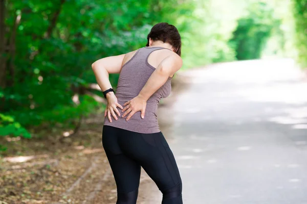 Woman with back pain, kidney inflammation, injury during workout, outdoors concept