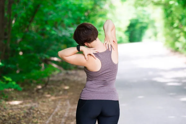 Woman with back pain, neck injury, trauma during workout, outdoors concept