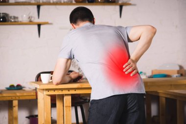 Sırt ağrısı, böbrek iltihabı, evde sırt ağrısı çeken bir adam, kırmızı ile işaretlenmiş acı veren bir bölge.