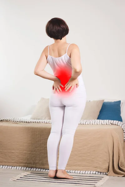Back pain, kidney inflammation, woman suffering from backache at home, painful area highlighted in red