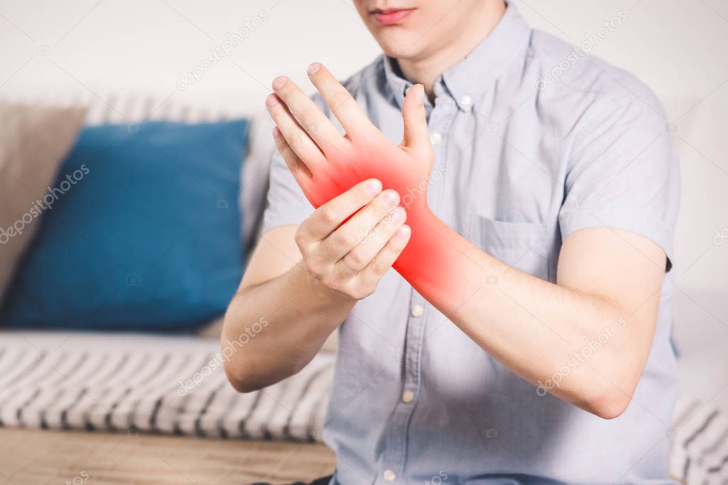 Pain in hand, man suffering from carpal tunnel syndrome at home, painful area highlighted in red