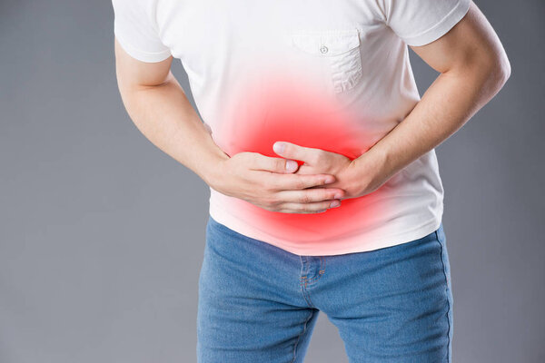 Man with abdominal pain, stomach ache on gray background, painful area highlighted in red