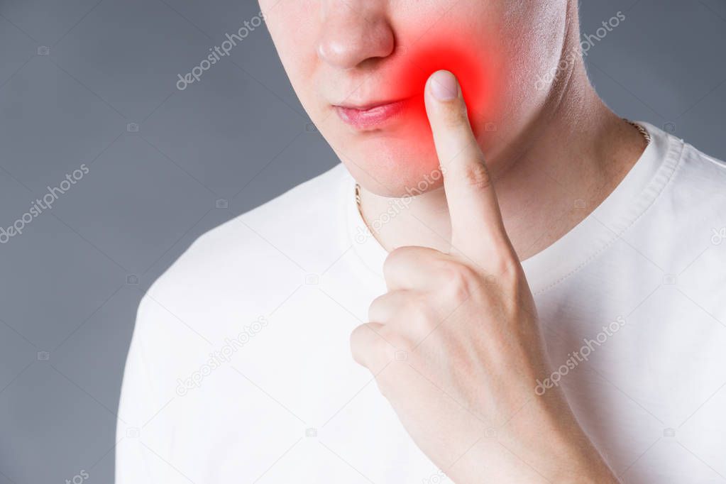 Man suffering from herpes virus on the lip, studio shot on gray background, painful area highlighted in red