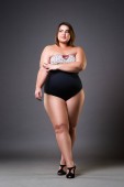 Plus Size Model im sexy Badeanzug, dicke Frau auf grauem Studiohintergrund, übergewichtiger weiblicher Körper, Ganzkörperporträt