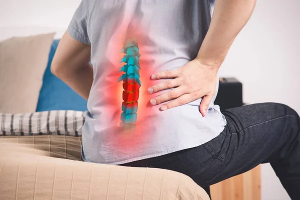 Pain in the spine, a man with backache at home, injury in the lower back, photo with highlighted skeleton — Stock Image Pain Spine Man Backache Home Injury Lower Back Photo Highlighted Royalty Free Stock Images