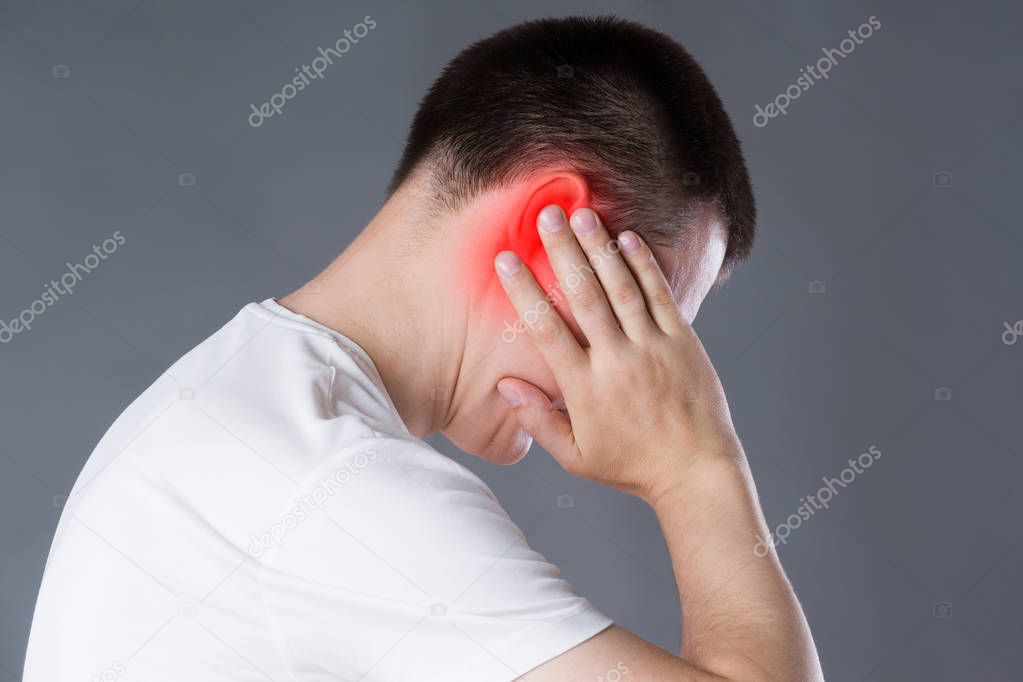 Man with earache, ear pain on gray background with red spot