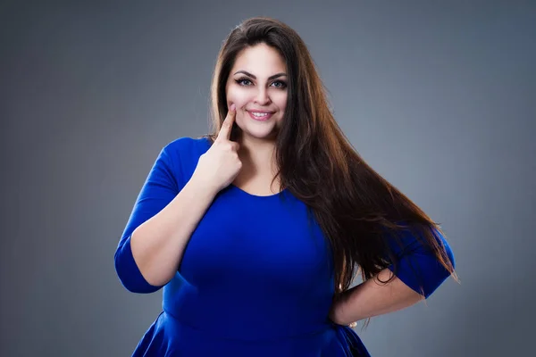 그녀의 플러스 스튜디오 배경에 파란색 드레스를 가리키는 뚱뚱한 — 스톡 사진