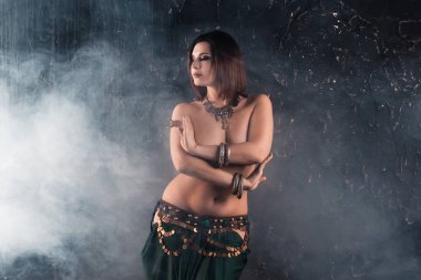 Seksi kadın koyu dumanlı arka plan, stüdyo çekim üzerinde etnik elbiseli oryantal dans gerçekleştirir