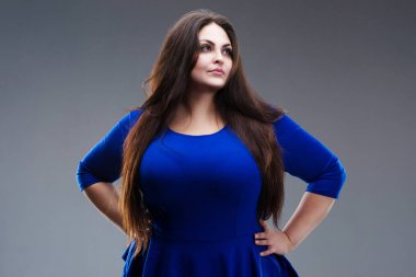 Artı boyutu moda model mavi elbiseli, gri arka plan üzerinde uzun saçlı şişman kadın esmer studio vurdu